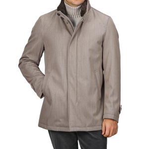 A person is dressed in a sophisticated and practical ensemble, featuring the Herno Light Brown Loro Piana Wool Twill Jacket with a high collar over a pure wool gray turtleneck sweater, paired with dark trousers. The rain-resistant jacket is buttoned up, showcasing its luxurious design.