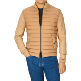 Man wearing a Herno Light Camel Wool Silk Nylon Padded Jacket and blue jeans, standing against a grey background. Only his torso and legs are visible.