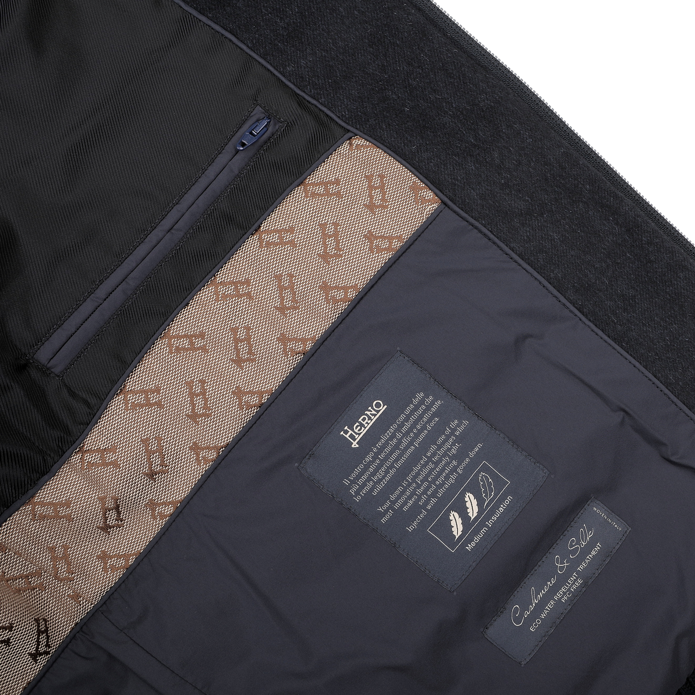 A close-up of the interior of the Herno Navy Blue Cashmere Silk Bomber Jacket reveals a lining adorned with patterns, labels, and pockets. The labels include care instructions and details about its luxurious cashmere and silk fabrics, as well as its water-repellent feature.