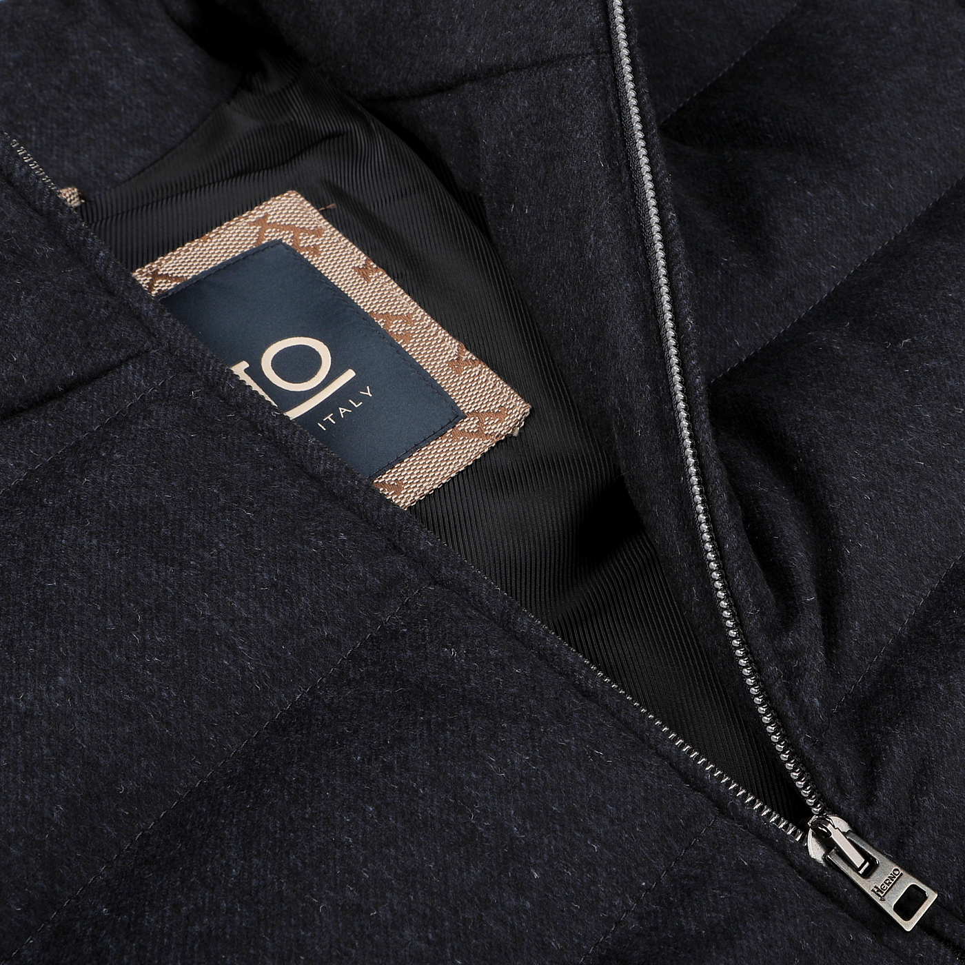 Close-up of a dark bomber jacket with a visible tag labeled "Herno, Italy" inside. The water-repellent Navy Blue Cashmere Silk Bomber Jacket is partially unzipped, revealing the tag.