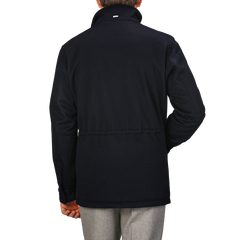 Rear view of a person wearing the Navy Blue Loro Piana Wool Field Jacket by Herno, featuring a high collar, paired with light gray pants, standing against a plain gray background.