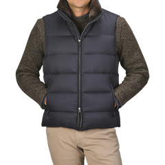 A person dressed in a Herno Navy Blue Nylon Goose Down Quilted Gilet over a brown sweater and khaki pants stands with their hands in the gilet pockets. The background is plain gray.