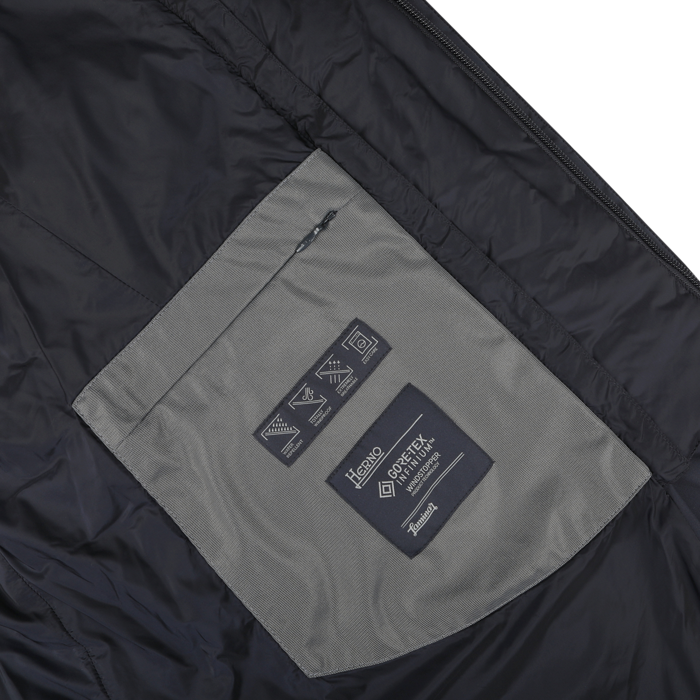 Close-up of the padded interior of the Herno Navy Blue Nylon Gore-Tex Laminar Coat, revealing a grey pocket with a zipper and multiple labels, including care instructions and a "Gore-Tex Infinium" tag.