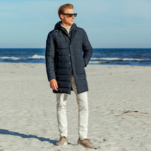 An outerwear specialist is standing on a beach wearing a Herno Navy Blue Nylon Gore-Tex Legend Coat.