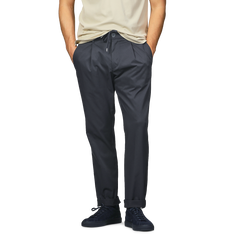 A person wearing a beige t-shirt, Herno's navy blue nylon stretch drawstring trousers, and black sneakers stands with hands in pockets.