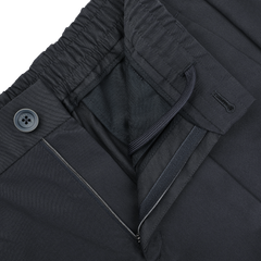 Close-up of slim fit navy blue nylon stretch trousers from Herno, featuring an elastic waistband with drawstring, button closure, and a visible zippered pocket.