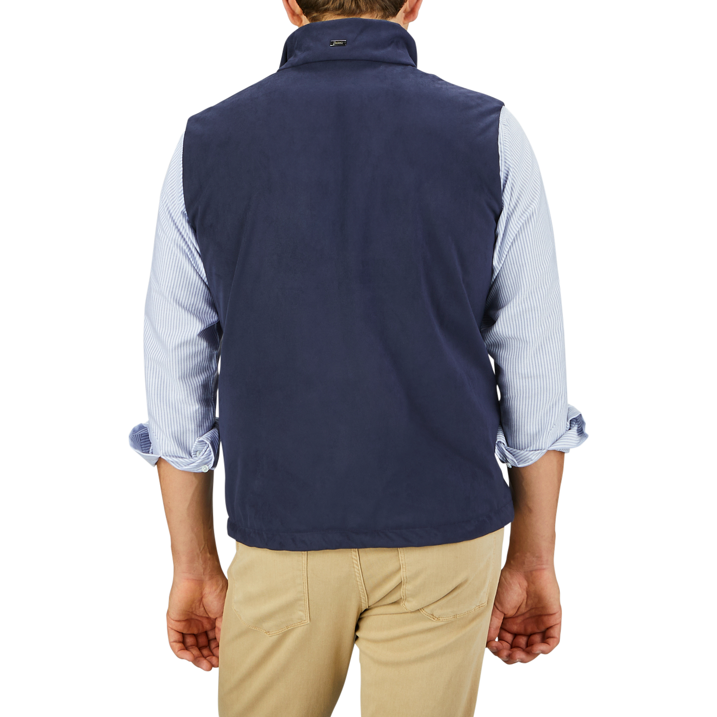 A man is shown from the back, wearing a Herno Navy Blue Suede Alcantara Zip Gilet over a light blue, rolled-up sleeve shirt and light khaki pants.
