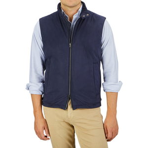 A person is wearing a Herno Navy Blue Suede Alcantara Zip Gilet, a light blue striped shirt with rolled-up sleeves, and beige pants against a light gray background.