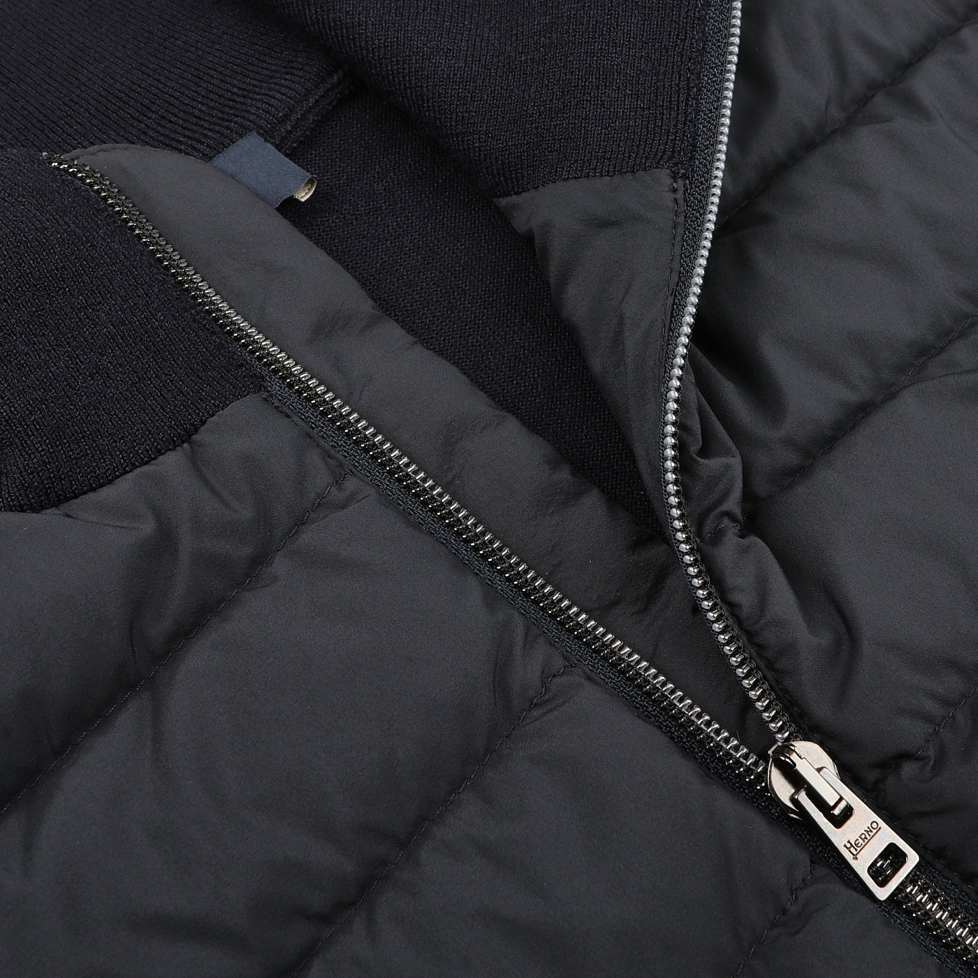 Close-up of Herno's Navy Blue Wool Silk Nylon Padded Jacket, featuring a partially open metallic zipper with a logo-engraved pull tab and a quilted fabric texture.