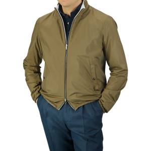 Man wearing a Herno olive green white reversible nylon blouson bomber jacket and blue trousers, hands in pockets, against a gray background. Head cropped from view.