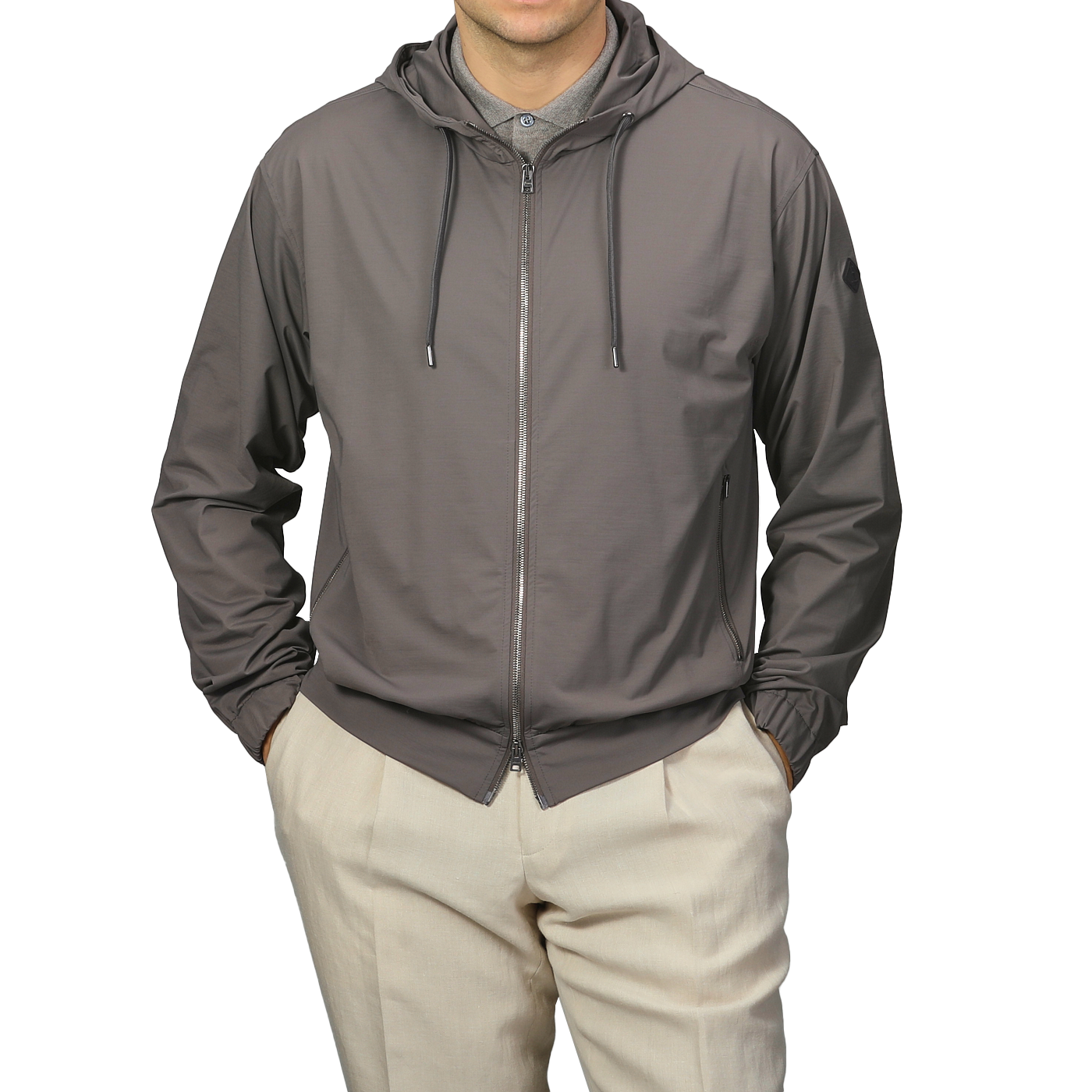 A person in a Herno Taupe Beige Nylon Jersey Hood Jacket and beige pants stands against a plain background, sporting the slim-fit, lightweight technical design of the zip-up hoodie.