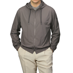 A person in a Herno Taupe Beige Nylon Jersey Hood Jacket and beige pants stands against a plain background, sporting the slim-fit, lightweight technical design of the zip-up hoodie.