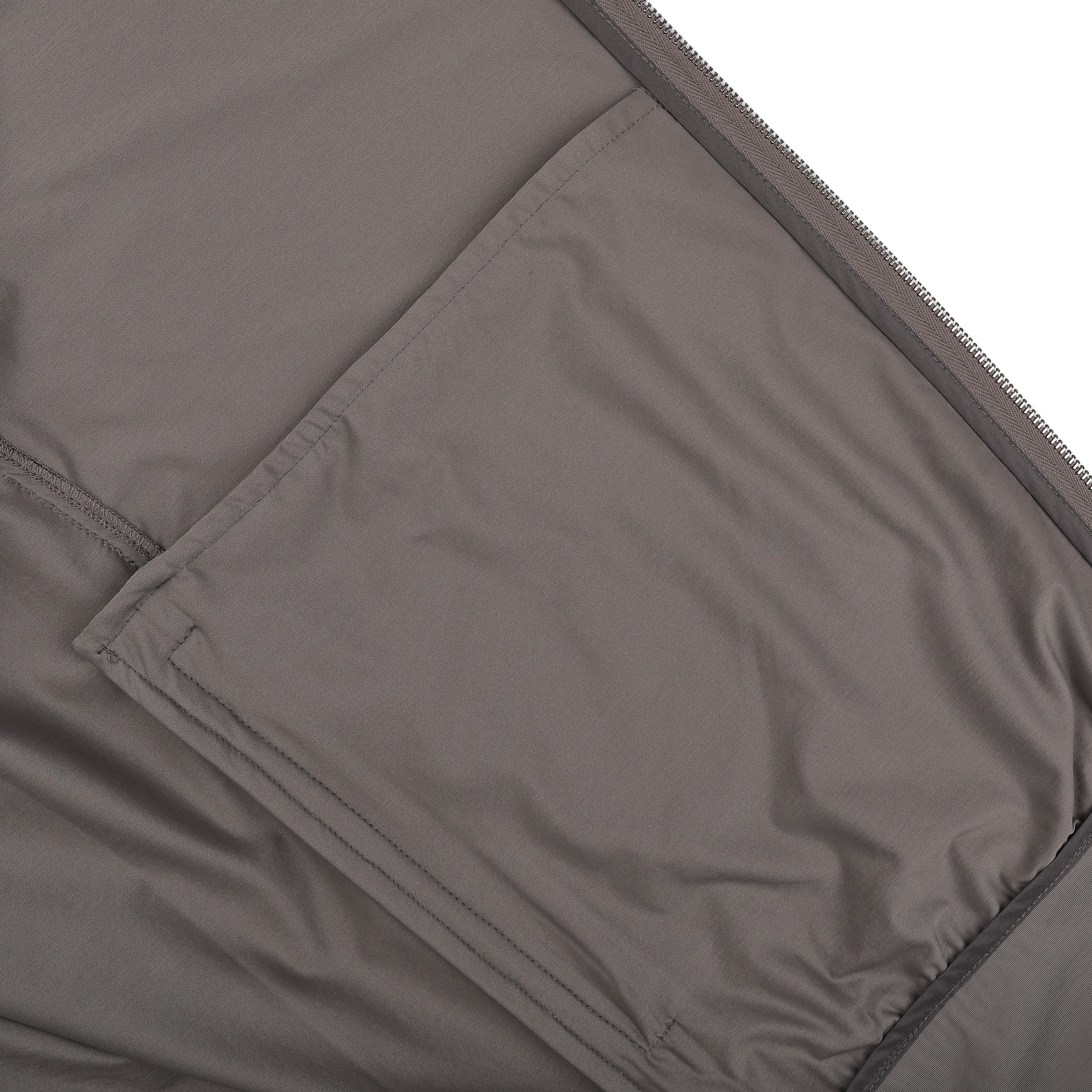 Close-up of a taupe beige fabric surface made from Herno's lightweight nylon jersey, featuring a stitched, rectangular pocket on the left side.