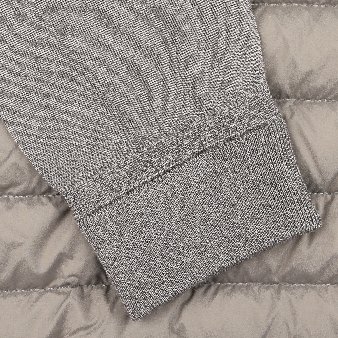 Close-up of a gray ribbed sweater sleeve, crafted with a luxurious wool-silk mix, resting on the Taupe Beige Wool Silk Nylon Padded Jacket by Herno.