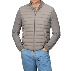 A person stands with hands in pockets, wearing a Herno Taupe Beige Wool Silk Nylon Padded Jacket over blue jeans against a neutral background.