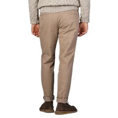 A person in Hiltl Beige Washed Cotton Gabardine Slim Chinos, a gray knit sweater, and brown shoes stands with their back to the camera.