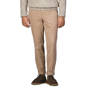 A person wearing a beige cable-knit sweater, Beige Washed Cotton Gabardine Slim Chinos by Hiltl, and dark brown shoes stands against a plain background.