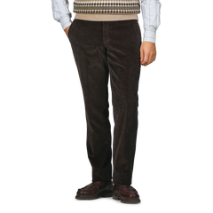 A person wearing Hiltl Brown Cotton Corduroy Regular Fit Chinos, a plaid shirt, a patterned sweater vest, and brown shoes stands against a plain background.