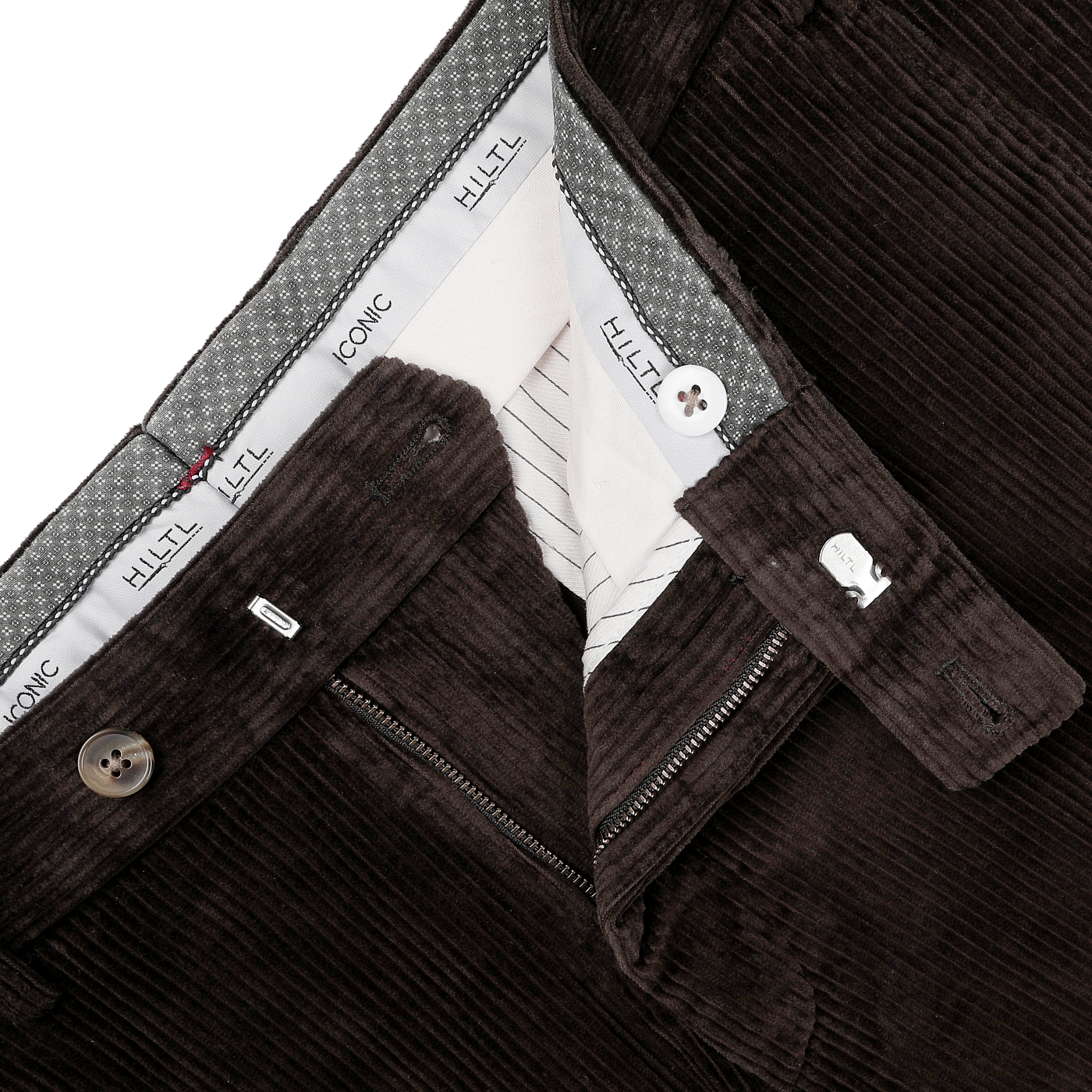 A close-up view of the Brown Cotton Corduroy Regular Fit Chinos shows a zipper and button closure. These chinos, designed for casual wear, have a waistband lined with checked fabric, featuring the "Hiltl" brand name on the inner waistband.