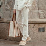 A man wearing Cream White Cotton Corduroy Regular Fit Chinos by Hiltl with a tan tote bag.