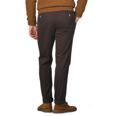 A person is shown from the back wearing Hiltl's Dark Brown Cotton Stretch Regular Fit Chinos paired with a brown sweater, with their hands in the chinos' pockets.