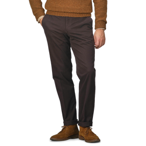 A person wearing a brown sweater, Hiltl dark brown cotton stretch regular fit chinos, and brown suede shoes stands with hands in pockets.