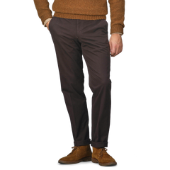 A person wearing a brown sweater, Hiltl dark brown cotton stretch regular fit chinos, and brown suede shoes stands with hands in pockets.