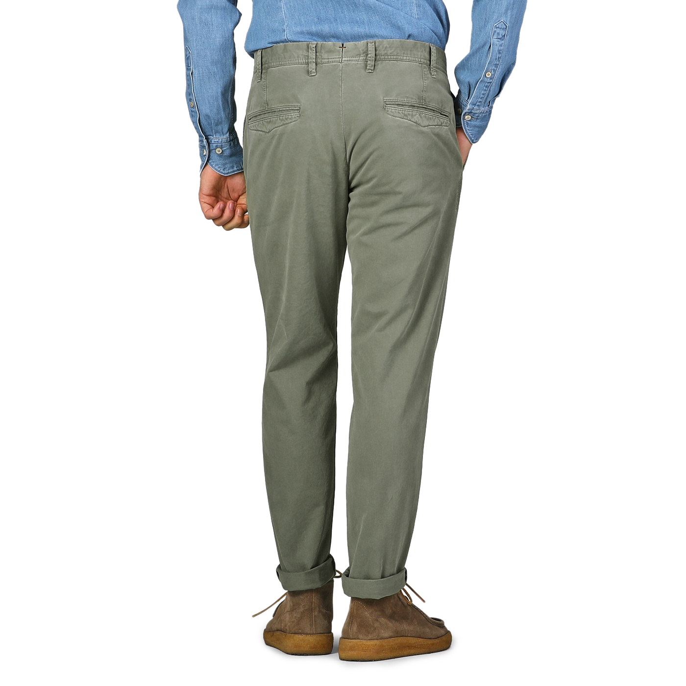 A person dressed in a blue shirt and Hiltl's Green Washed Cotton Gabardine Slim Chinos, seen from behind with hands tucked in pockets against a plain backdrop.