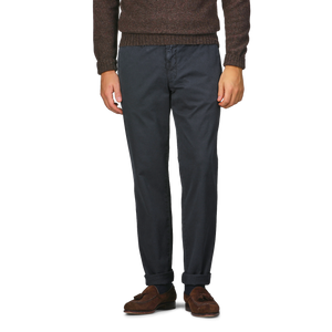 A person wearing a brown sweater, Navy Washed Cotton Gabardine Slim Chinos by Hiltl, and brown loafers stands against a plain background.