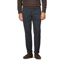 A person wearing a brown sweater, Navy Washed Cotton Gabardine Slim Chinos by Hiltl, and brown loafers stands against a plain background.