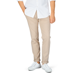 A person standing in a white shirt, Hiltl sand beige cotton nylon slim chinos, and white shoes against a gray background.