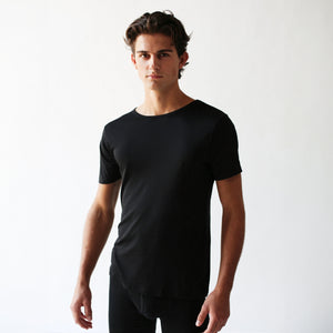 The individual is posed against a simple white backdrop, wearing a stylish black slim fit crewneck t-shirt from The White Briefs, the Earth Organic Pima Cotton Crewneck T-shirt.