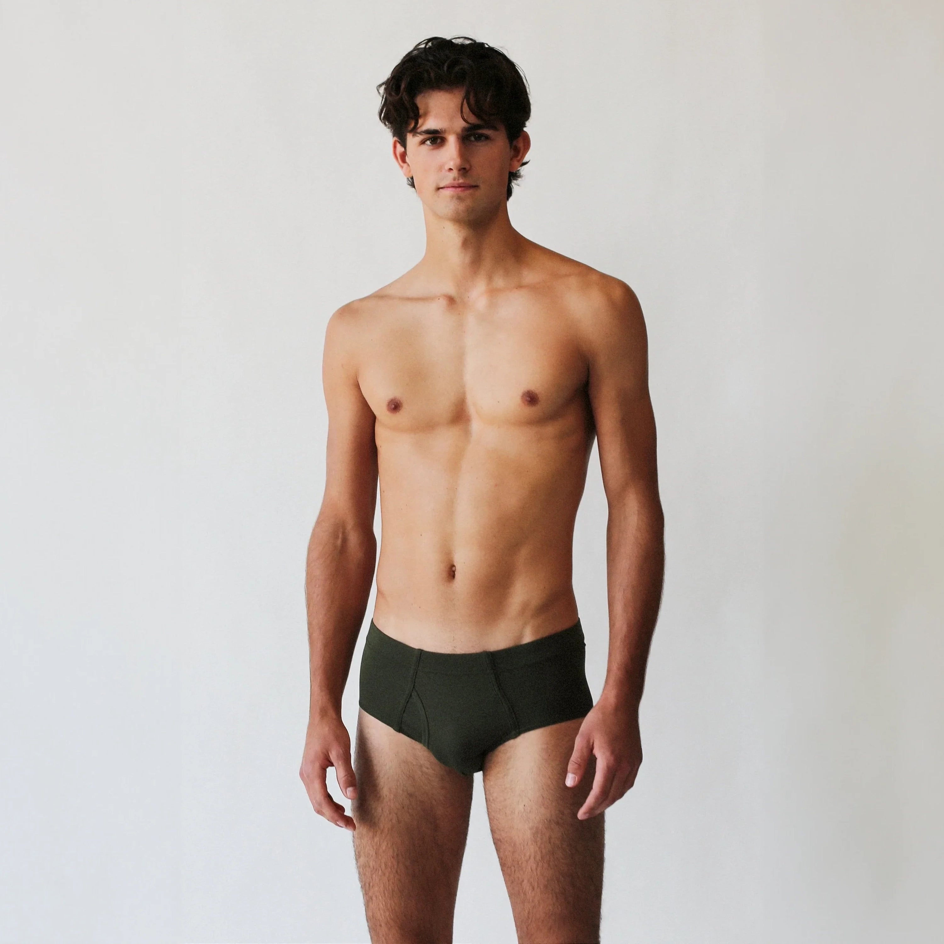 A man with dark hair stands against a plain background wearing the Rio Pima Cotton Lyocell Briefs from The White Briefs, designed in dark green and made from a luxurious blend of lyocell and Pima cotton.