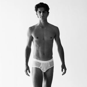 A person models the Platan Organic Cotton Mesh Briefs from The White Briefs in a black and white photo, gazing ahead against a plain background.