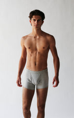 A man stands confidently against a plain background, wearing The White Briefs' Wil Organic Pima Cotton Trunks.