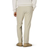 Person wearing Incotex Beige Cotton Corduroy High Comfort Chinos, a white sweater, and matching beige shoes is shown from the back, standing against a plain background.