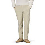 A person wearing Incotex Beige Cotton Corduroy High Comfort Chinos, a white sweater, and beige shoes stands with hands in pockets against a neutral background.