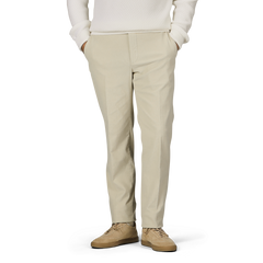 A person wearing Incotex Beige Cotton Corduroy High Comfort Chinos, a white sweater, and beige shoes stands with hands in pockets against a neutral background.