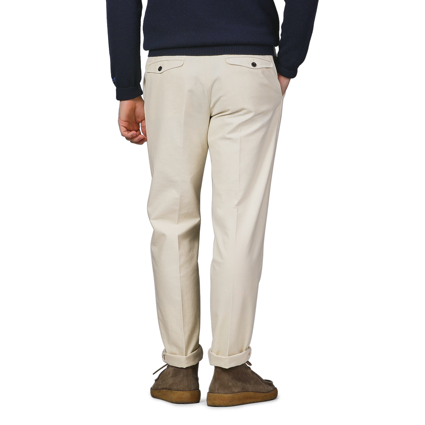 A person wearing Incotex's Cream White Cotton Twill Pleated Chinos, brown shoes, and a dark sweater stands with their back to the camera.