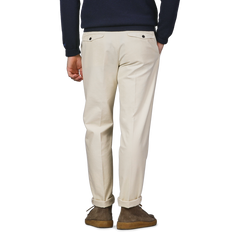 A person wearing Incotex's Cream White Cotton Twill Pleated Chinos, brown shoes, and a dark sweater stands with their back to the camera.