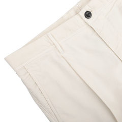 Close-up of Cream White Cotton Twill Pleated Chinos by Incotex, featuring a black button and side pocket, resting on a white surface.