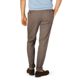 Man wearing dark brown Incotex cotton stretch regular chinos and brown shoes against a blue background.