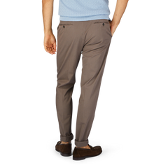 Man wearing dark brown Incotex cotton stretch regular chinos and brown shoes against a blue background.