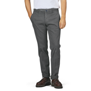 A person wearing Incotex Dark Grey Cotton Stretch Model 30 Chinos, alongside a white shirt and brown shoes, stands with hands in pockets against a plain background.