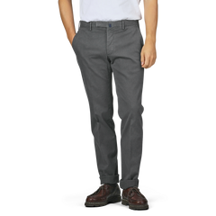 A person wearing Incotex Dark Grey Cotton Stretch Model 30 Chinos, alongside a white shirt and brown shoes, stands with hands in pockets against a plain background.