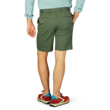 Man standing from behind wearing a blue shirt, Grass Green Cotton Royal Batavia Shorts by Incotex, and colorful sneakers.