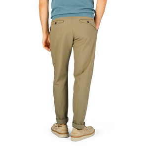 A person standing in Incotex Grass Green Cotton Stretch Pleated Chinos and beige sneakers against a blue background.