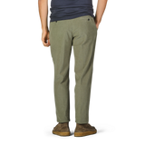 A person stands wearing Incotex Green Cotton Corduroy High Comfort Chinos, a dark blue shirt, and brown shoes. The individual is facing away from the camera with hands in the chinos' pockets.