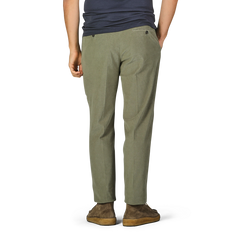 A person stands wearing Incotex Green Cotton Corduroy High Comfort Chinos, a dark blue shirt, and brown shoes. The individual is facing away from the camera with hands in the chinos' pockets.