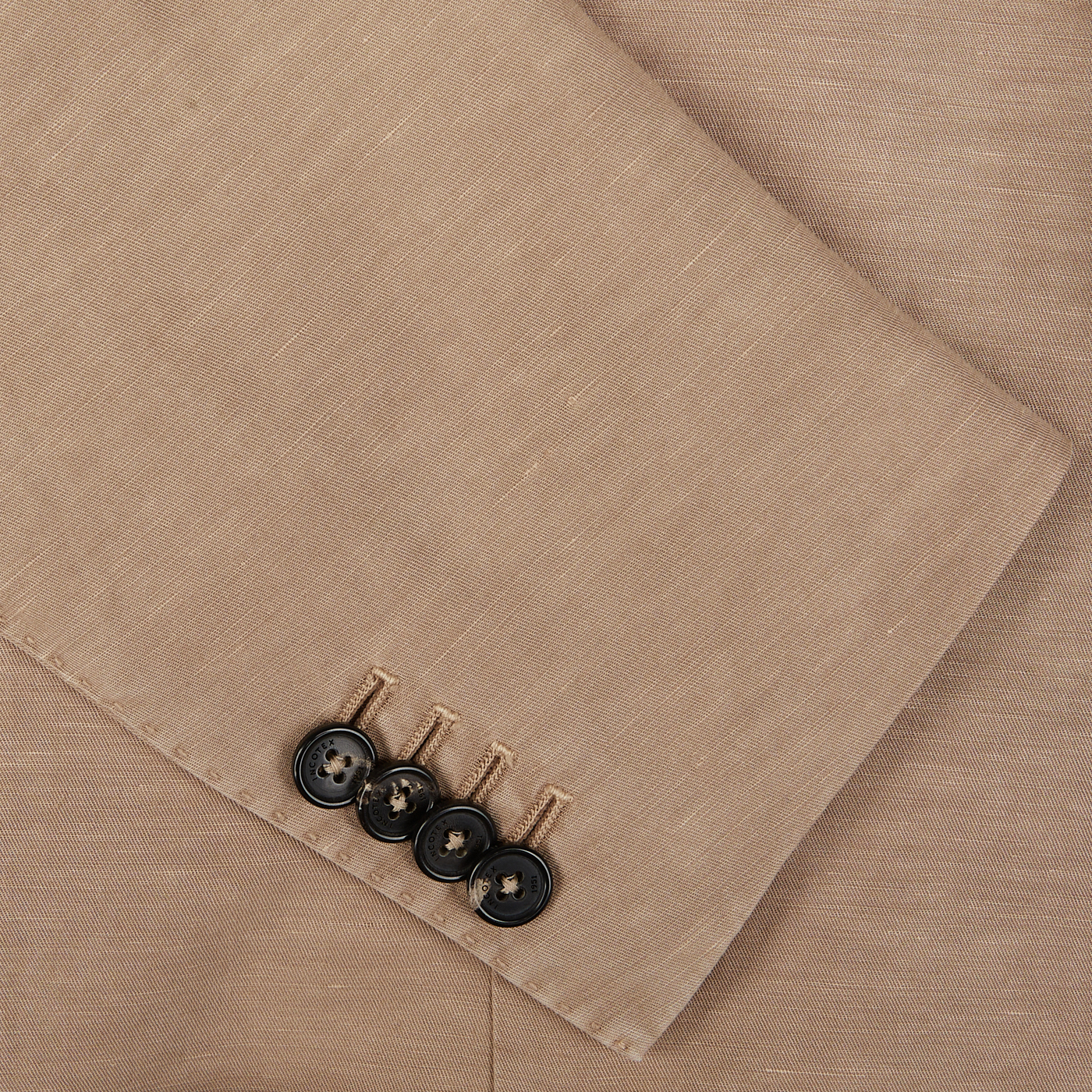 Four black buttons and matching thread on a piece of Slowear Light Beige Washed Chinolino Suit fabric, perfect for an unstructured jacket.